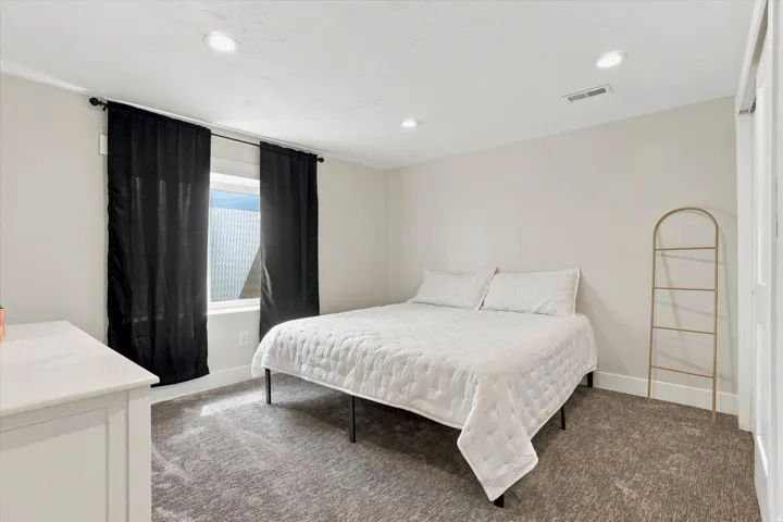 Carpeted room featuring a window with black curtains, recessed lighting, and a white dresser
