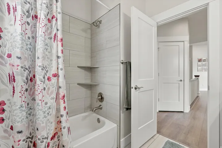 Bathroom featuring a full tub with brushed nickel fixtures, tiled shower surround, and built-in corner shelving
