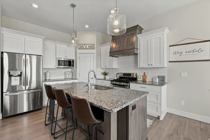 Kitchen featuring a large island with a composite countertop, white shaker cabinetry, stainless steel appliances, and wood-finish flooring