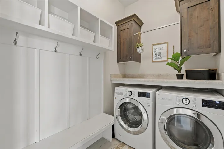 Dedicated laundry area featuring white shaker-style cabinetry, a built-in bench, and coat hooks