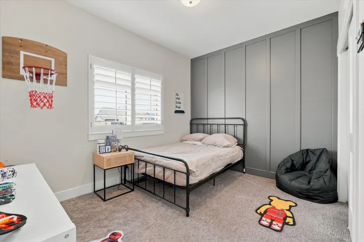 Bedroom featuring a paneled accent wall, neutral carpeting, and a window with plantation shutters