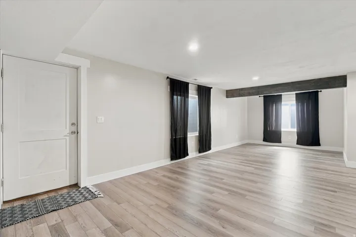 Spacious room featuring light wood-finish flooring, recessed lighting, and a prominent exposed beam detail