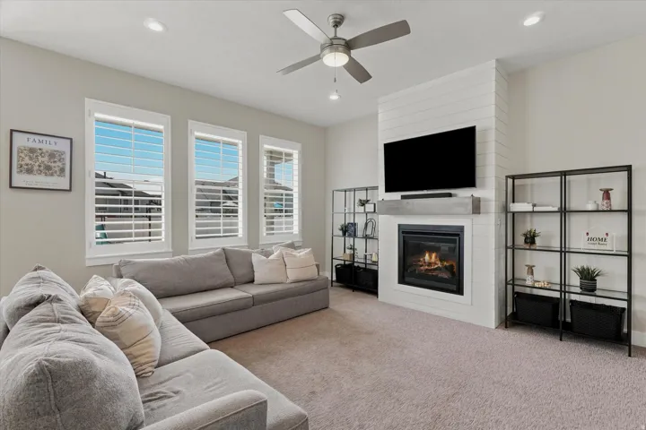 Spacious living area featuring a fireplace with a shiplap accent wall, built-in shelving, a ceiling fan, recessed lighting, and triple windows with plantation shutters