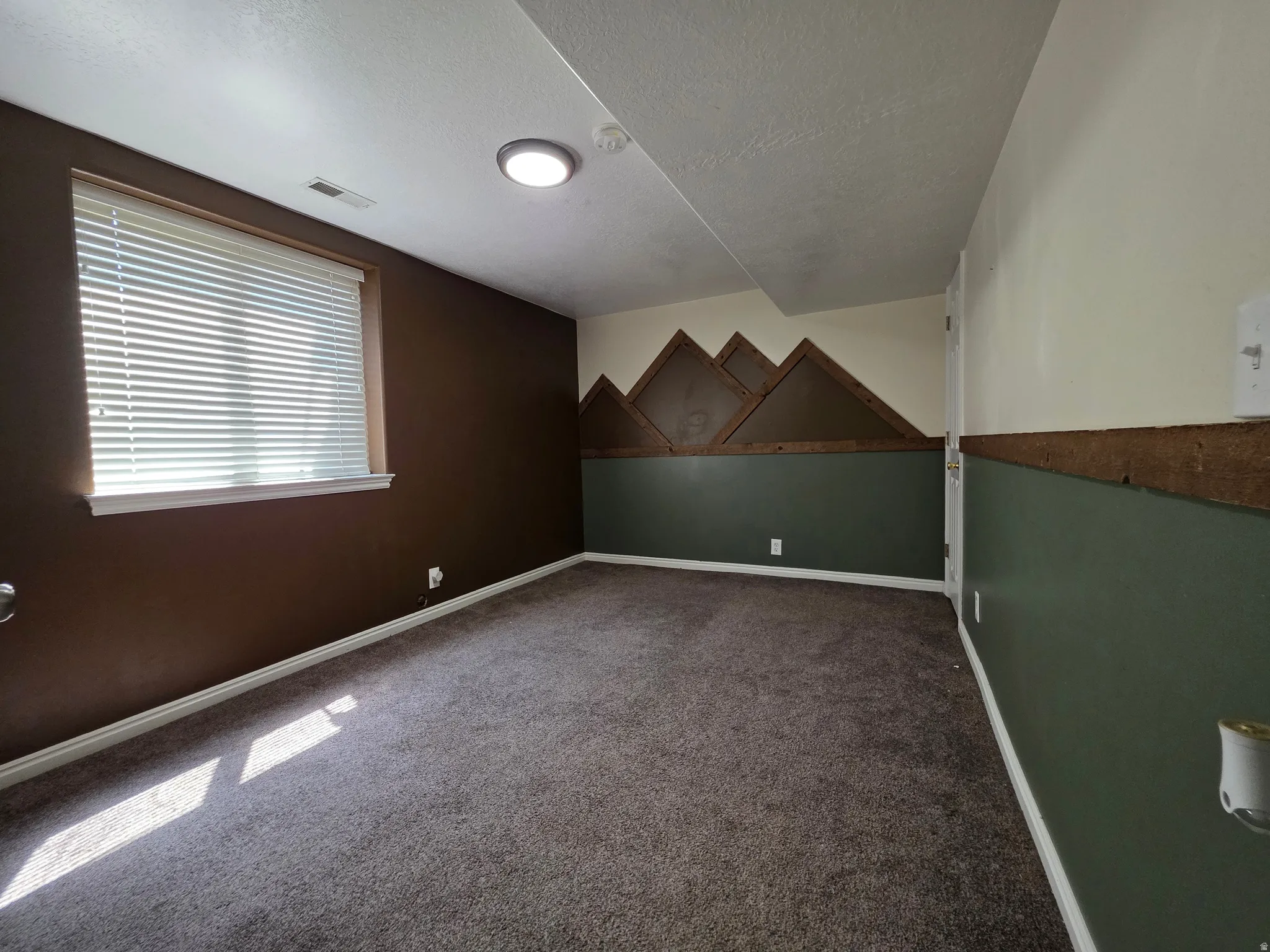 Carpeted room featuring a window with horizontal blinds, overhead flush-mount lighting, and two-tone wall finishes