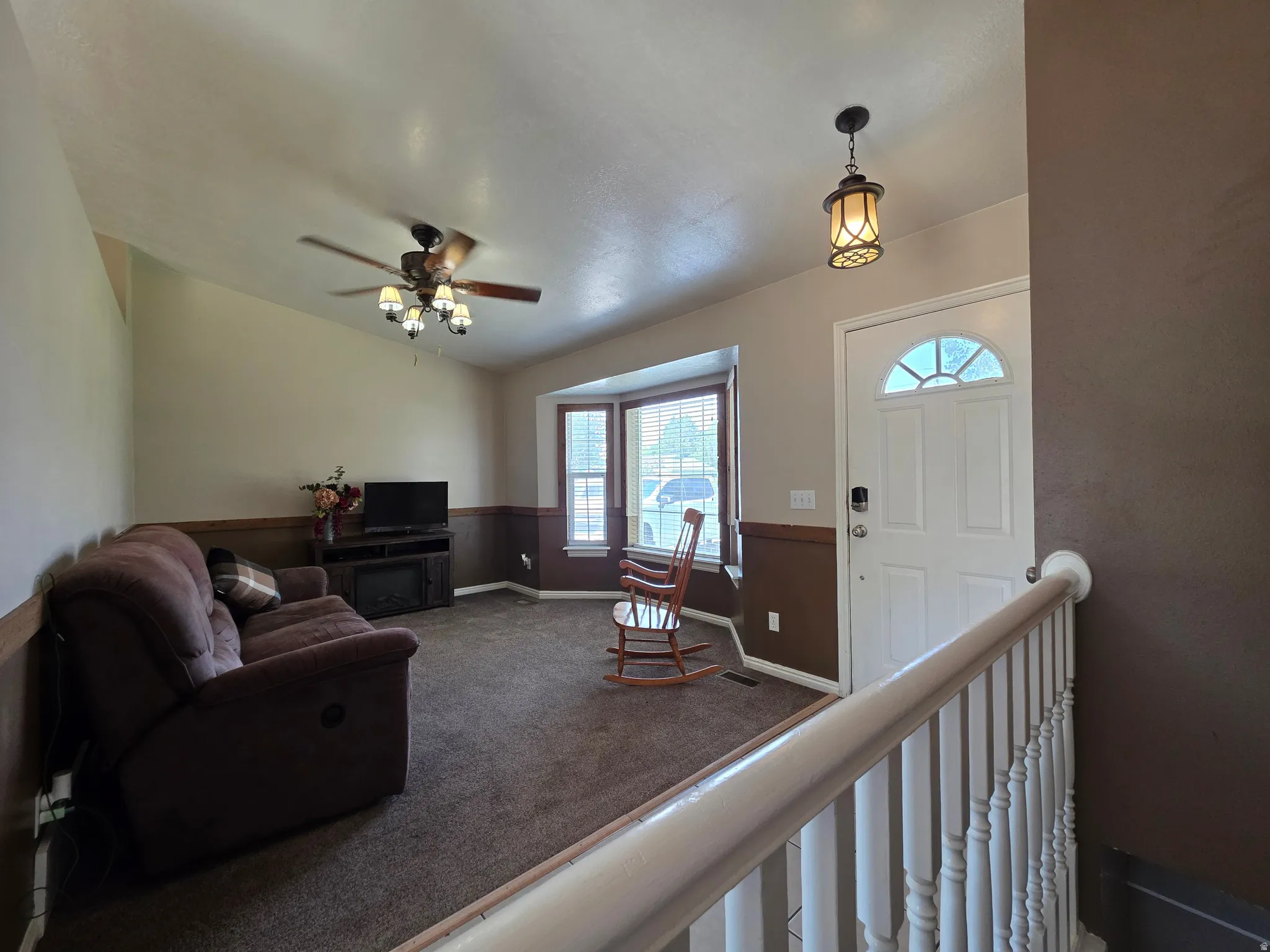 Entryway and living area featuring a white front door with an arched window, a decorative pendant light, and a white baluster railing