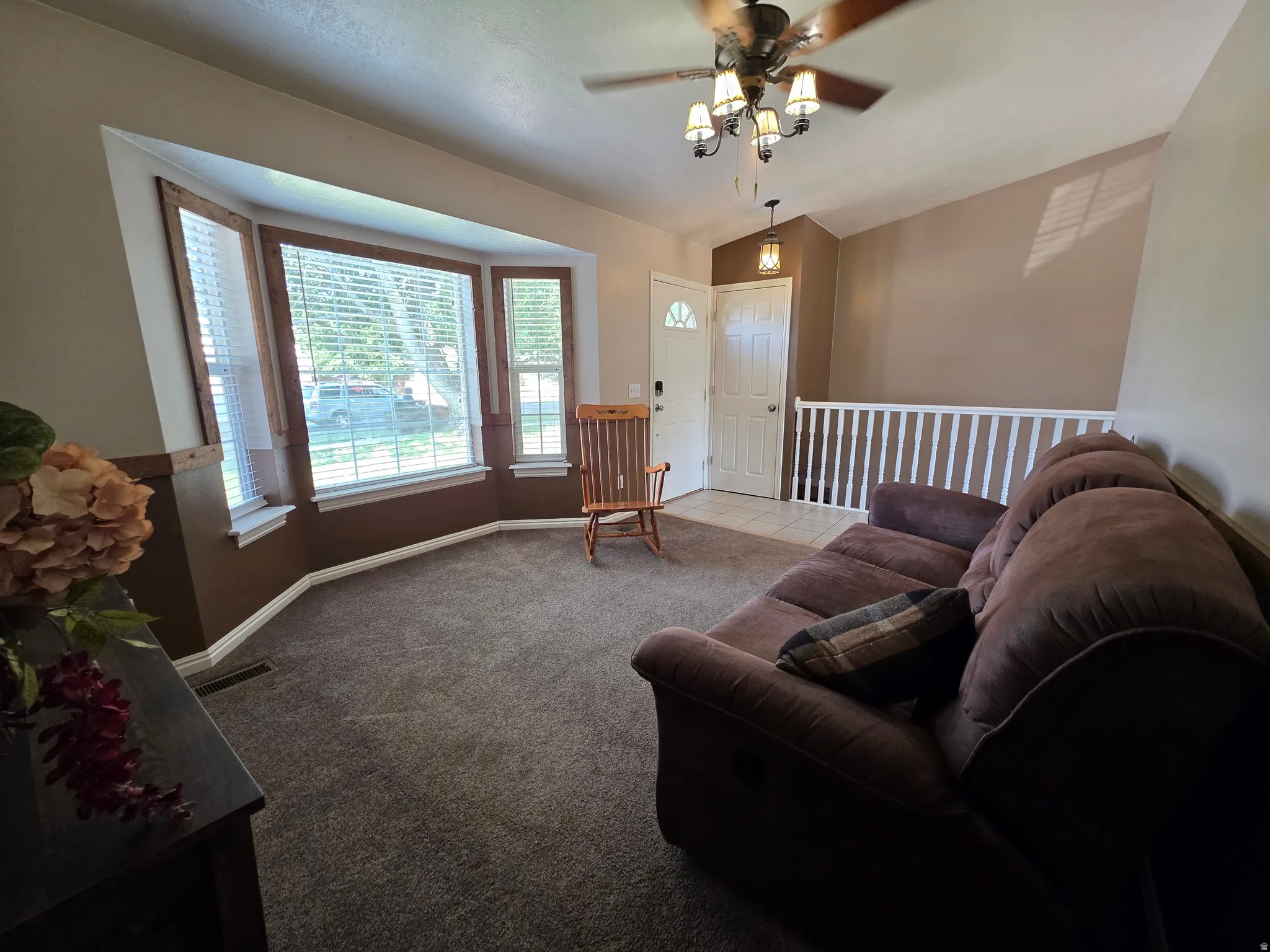 Living area with bay windows, carpeted flooring, and a ceiling fan with integrated lighting