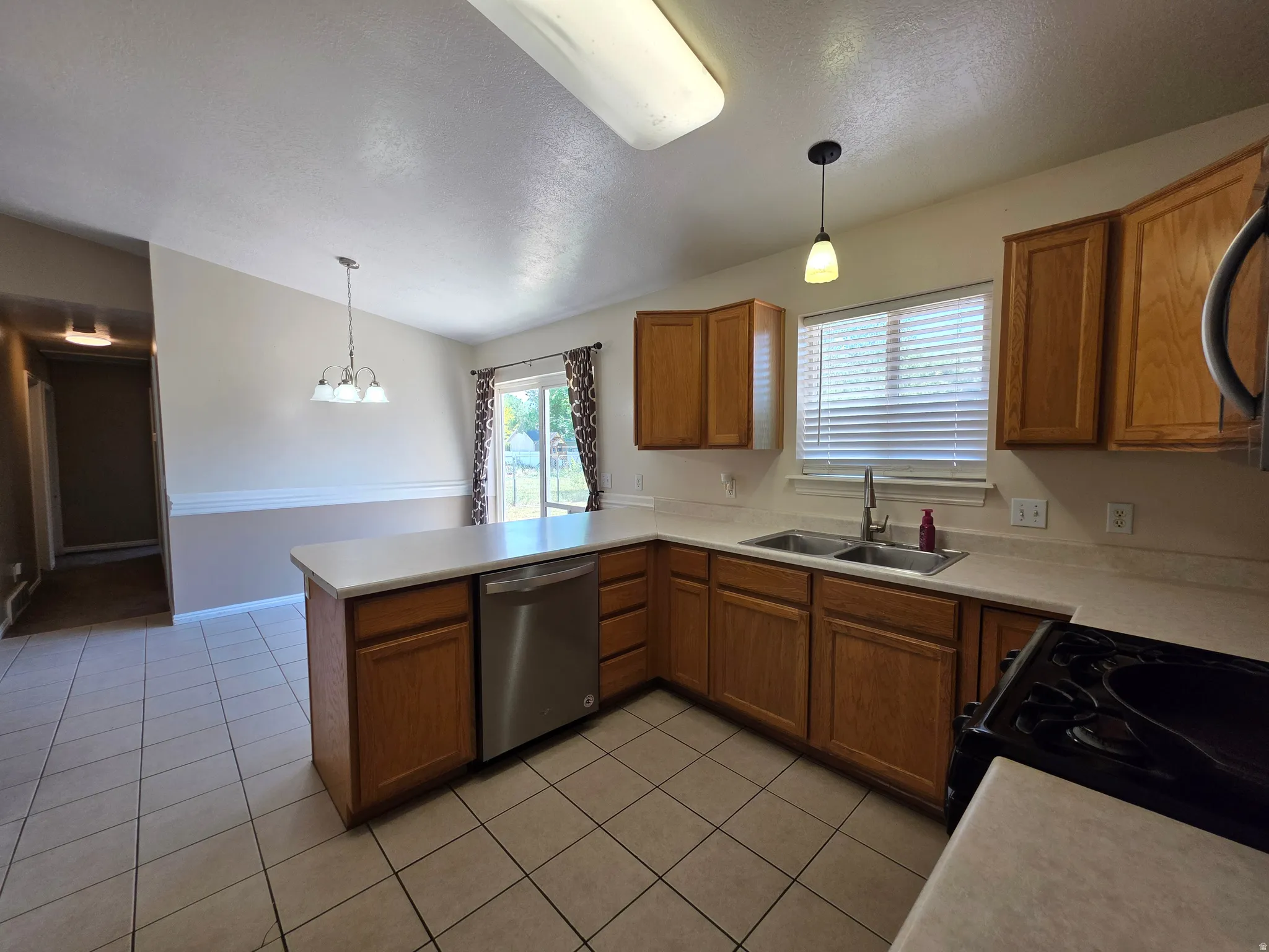 Functional kitchen featuring tile flooring, light wood cabinetry, laminate countertops, a stainless steel dishwasher, and a double basin sink