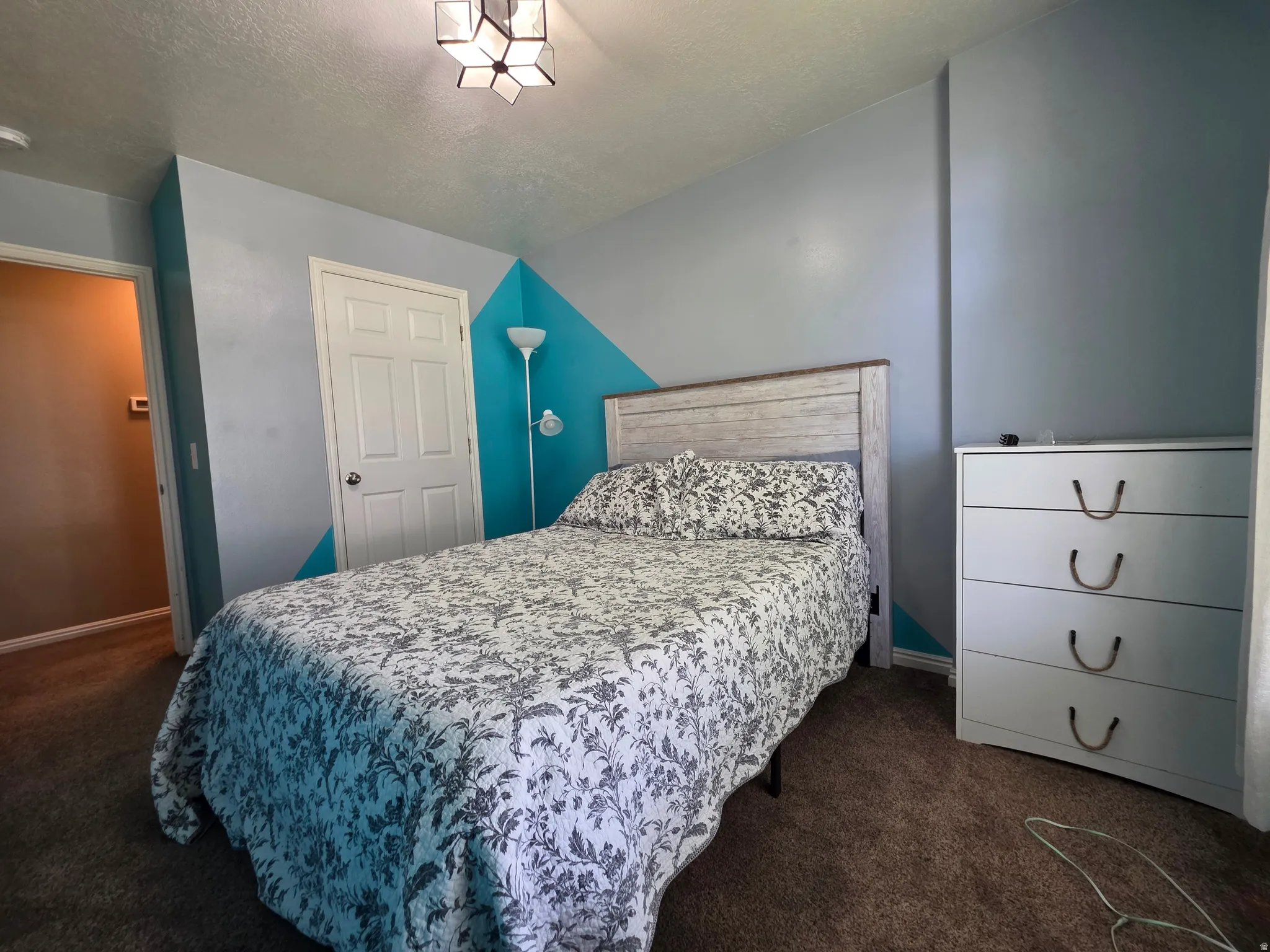 Bedroom featuring brown carpet flooring, a white paneled door, and a geometric accent wall
