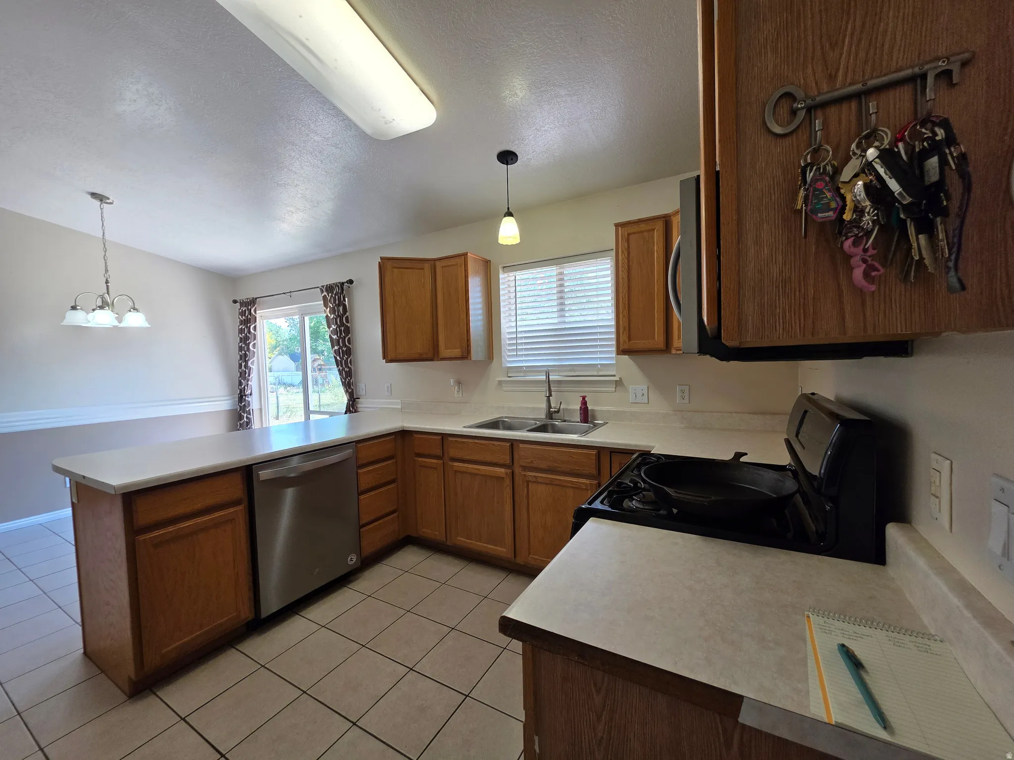 Kitchen featuring wood-finish cabinetry, tile flooring, light-toned countertops, and a stainless steel dishwasher