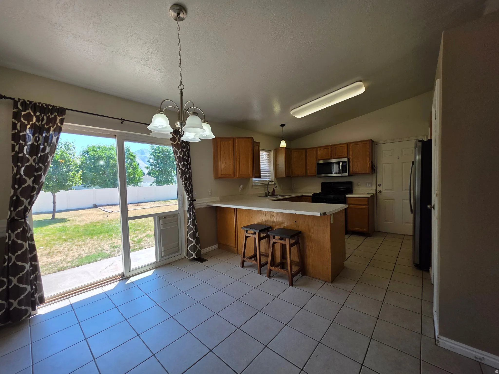 Kitchen and dining area featuring tile flooring, light wood cabinetry, white countertops, and stainless steel appliances