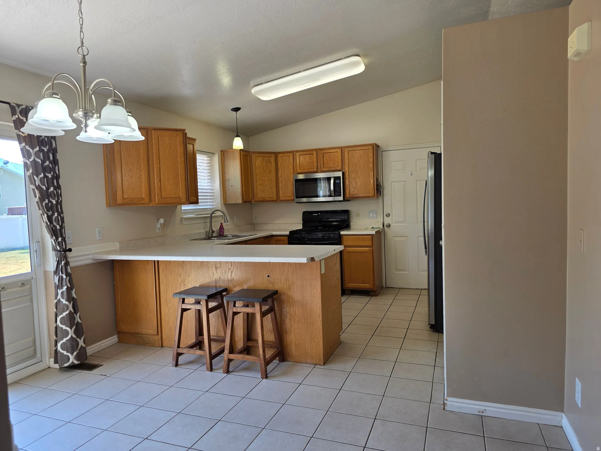 Kitchen featuring wood cabinetry, white tile flooring, stainless steel appliances, a breakfast bar, and vaulted ceilings