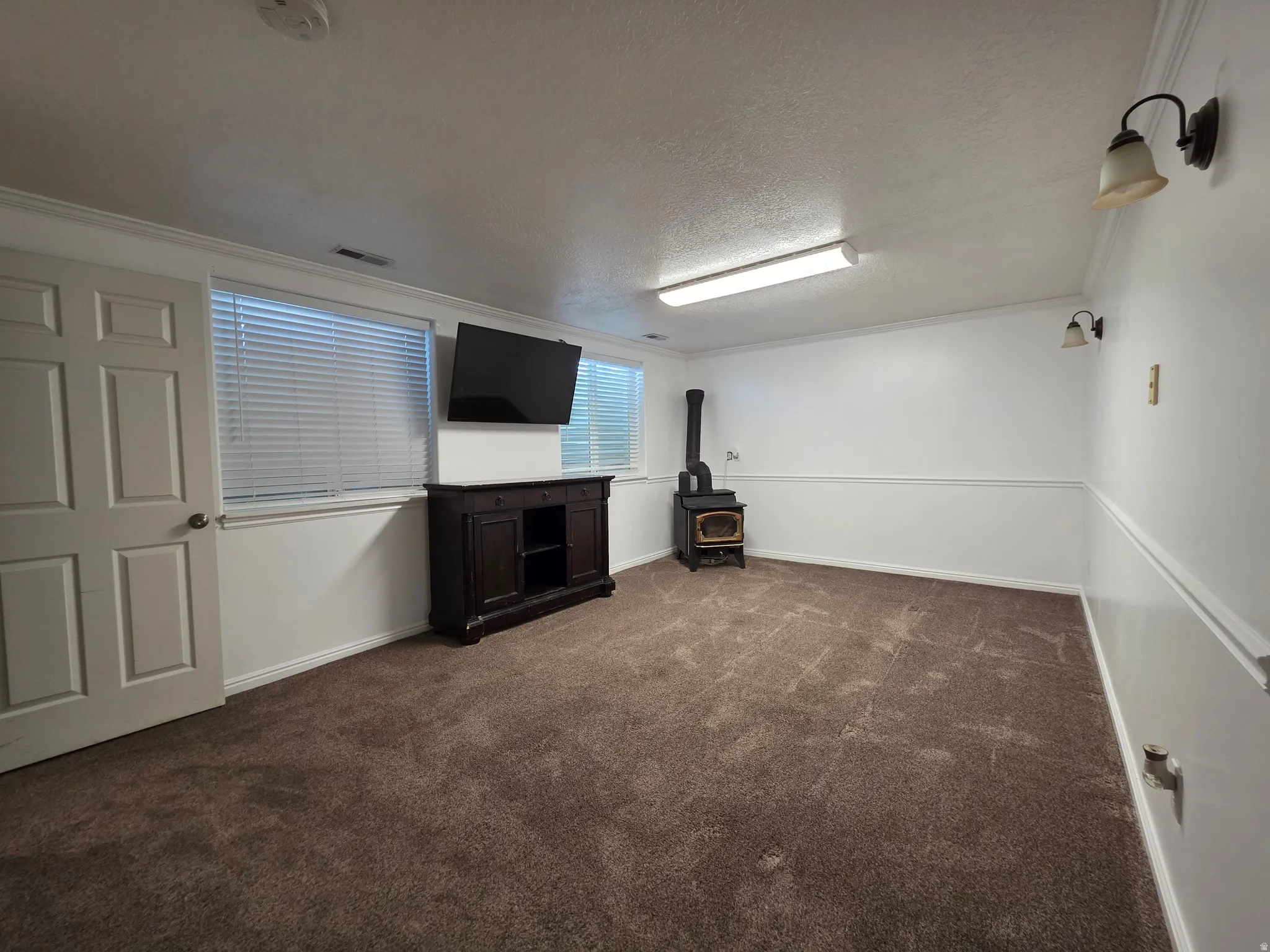 Spacious room featuring broadloom carpet, white walls with wainscoting, and a prominent wood-burning stove