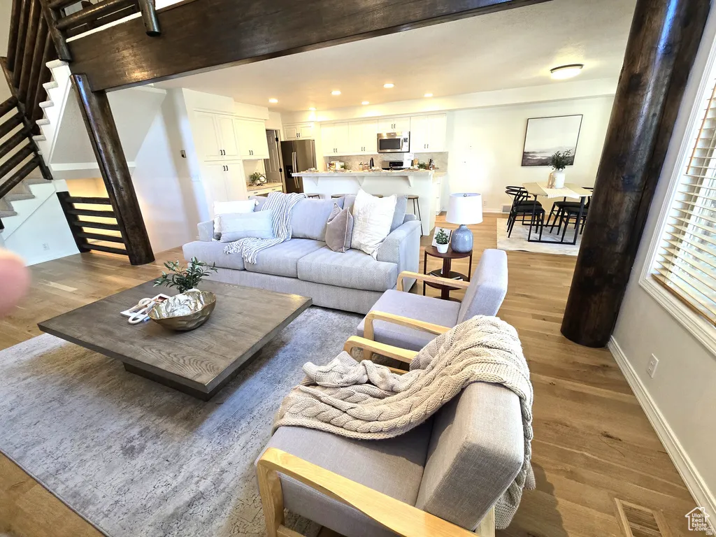 Open-concept living area featuring wood-finish flooring, exposed timber beams, and a modern staircase with horizontal railings