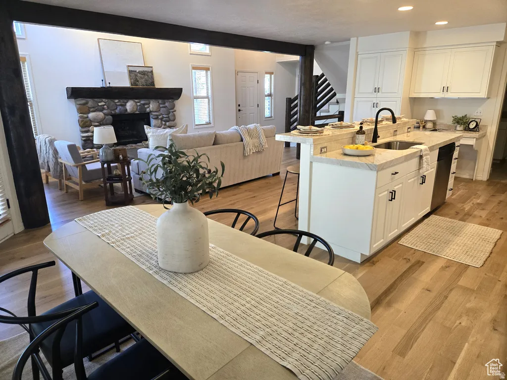 Open-concept living space featuring wood-finish flooring, a stone fireplace, and exposed wood beams