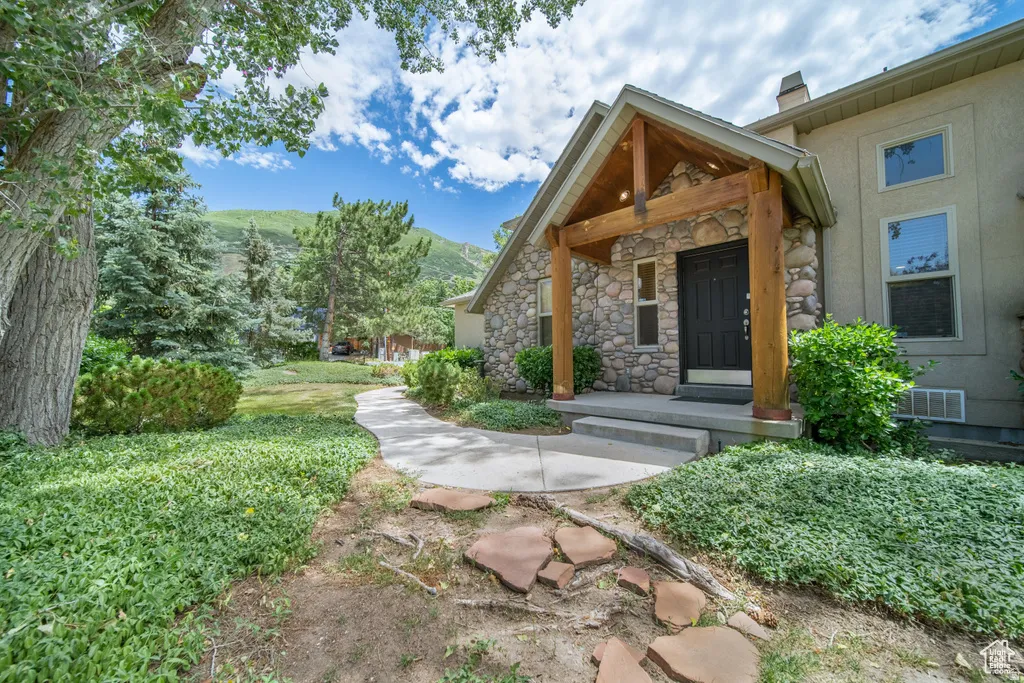 Stone facade home featuring a prominent wood beam porch, dark entry door, and multi-pane windows