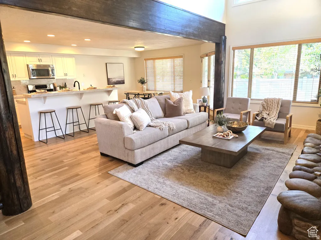 Open-concept living space featuring wood-finish flooring, a kitchen island with seating, white cabinetry, and stainless steel appliances