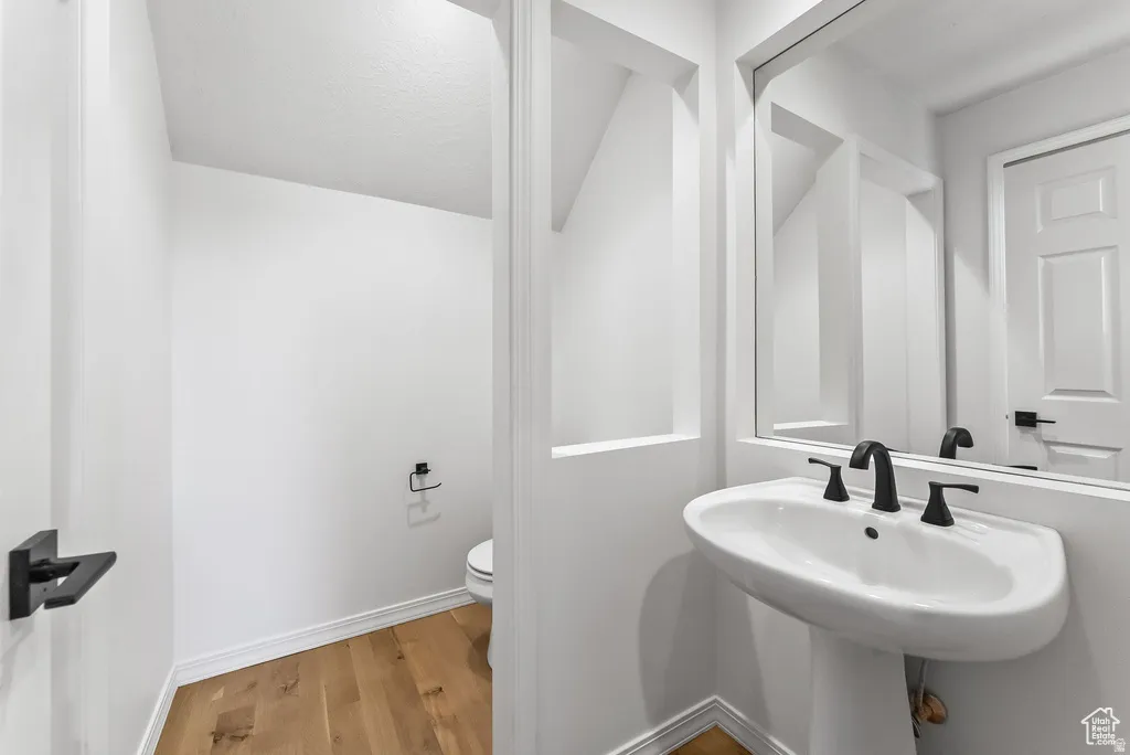 Pedestal sink with matte black faucet, wall-mounted mirror, and warm wood-finish flooring