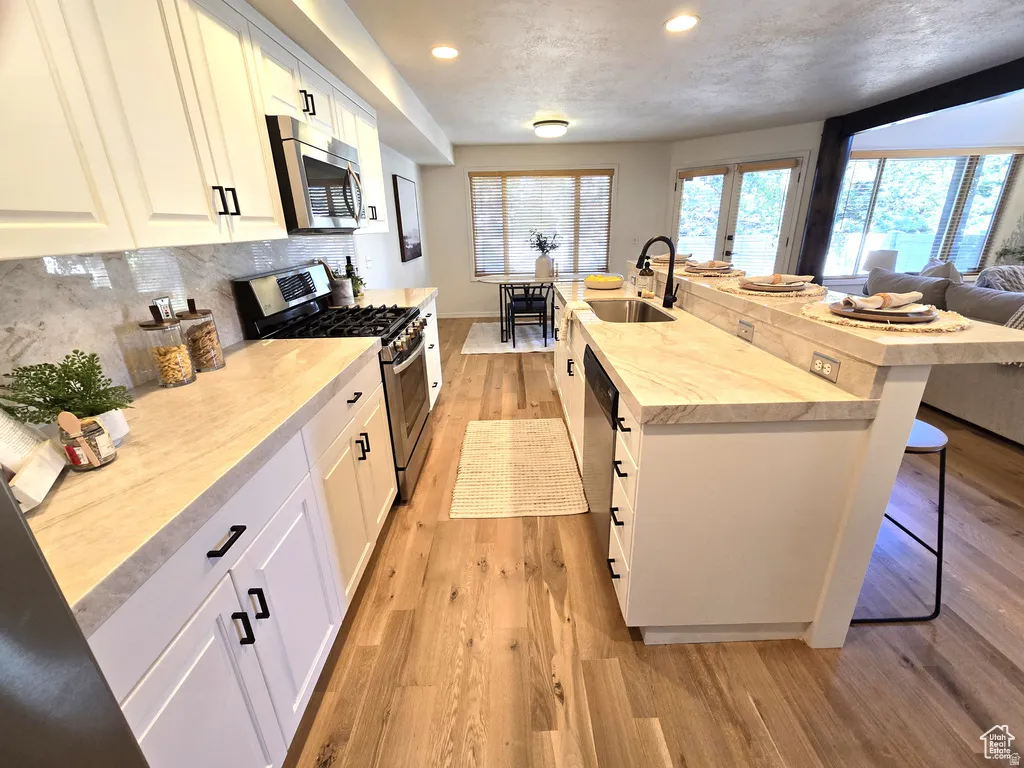 Open-concept kitchen featuring wood-finish flooring, white cabinetry, integrated stainless steel appliances, a light-toned countertop, and a breakfast bar