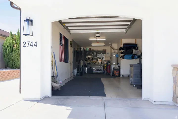 Attached two-car garage featuring a concrete floor, built-in storage shelves, fluorescent lighting, and a water heater