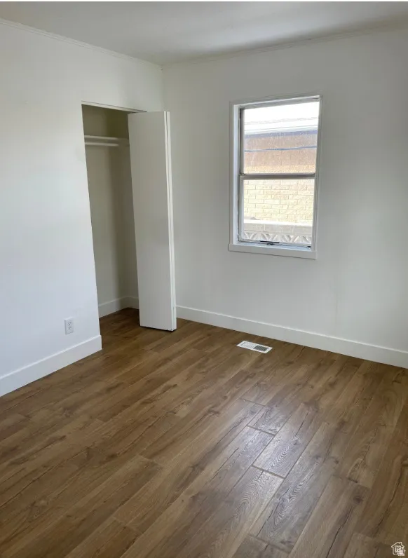 Light-filled room featuring wood-finish flooring, white walls, a double-hung window, and an open closet with hanging rod