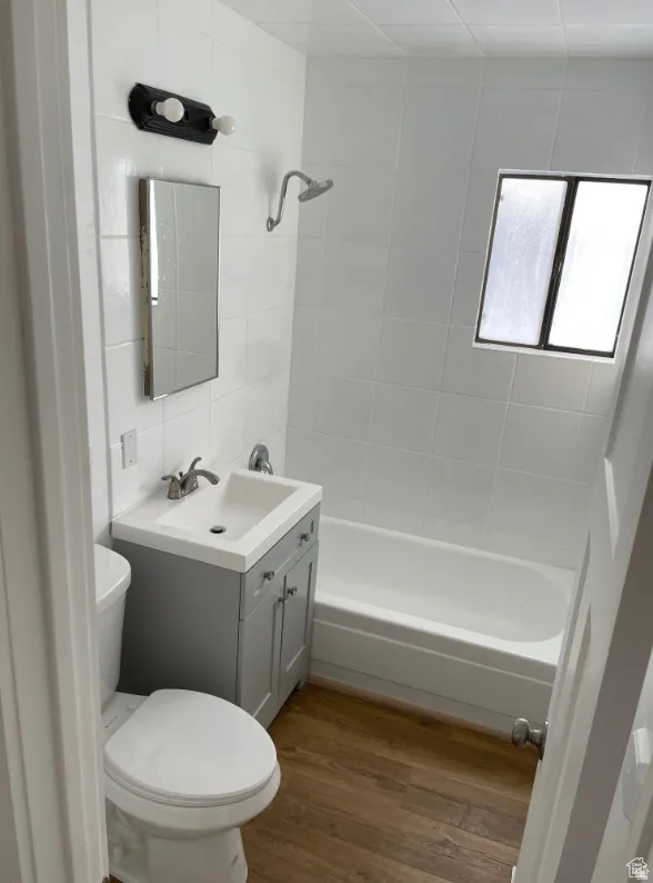 Bathroom featuring wood-finish flooring, a white tiled shower surround, a compact vanity with basin sink, a wall-mounted medicine cabinet, and an integrated bathtub