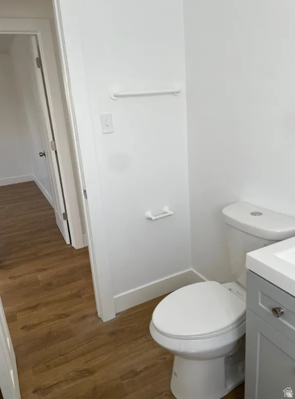 Bathroom featuring wood-finish flooring, a white toilet, a grey vanity with a white countertop, and white baseboards