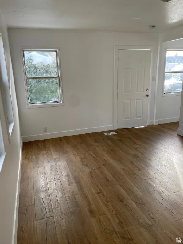 Spacious room featuring wood-finish flooring, white walls, and a paneled entry door