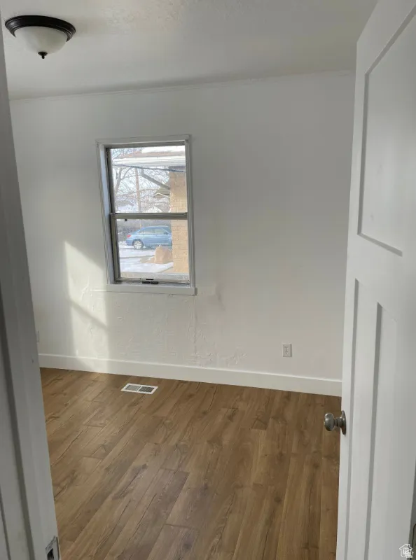 Room featuring wood-finish flooring, white baseboards, a single window, and a flush mount ceiling light fixture