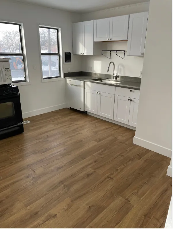 Kitchen with wood-finish flooring, white cabinetry, dark countertops, and stainless steel sink with a gooseneck faucet