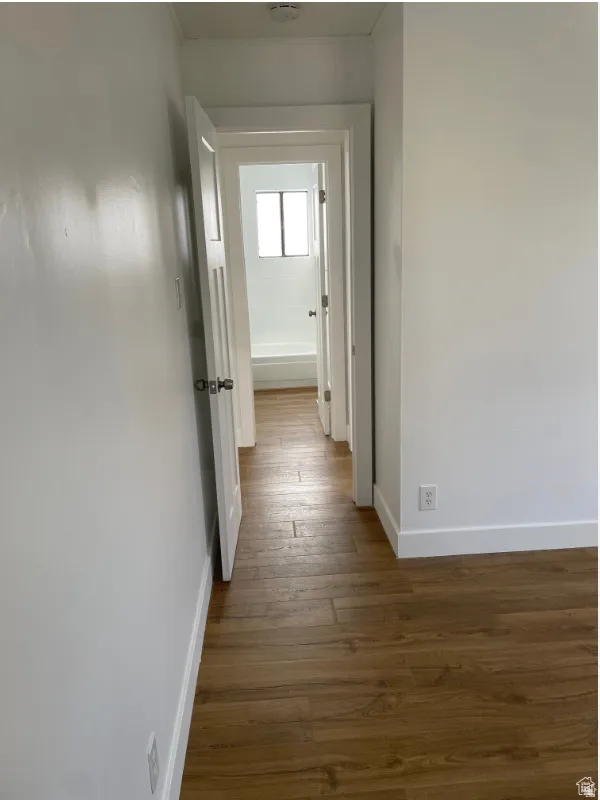 Hallway with wood-finish flooring, leading to a bathroom featuring a white tub and tiled surround