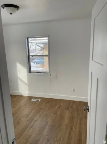 Room featuring wood-finish flooring, white baseboards, a single window, and a flush mount ceiling light fixture