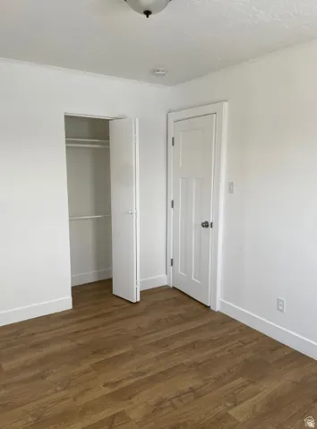 Room featuring wood-finish flooring, white baseboards, a flush-mount ceiling light, a built-in closet with bifold doors, and a paneled interior door