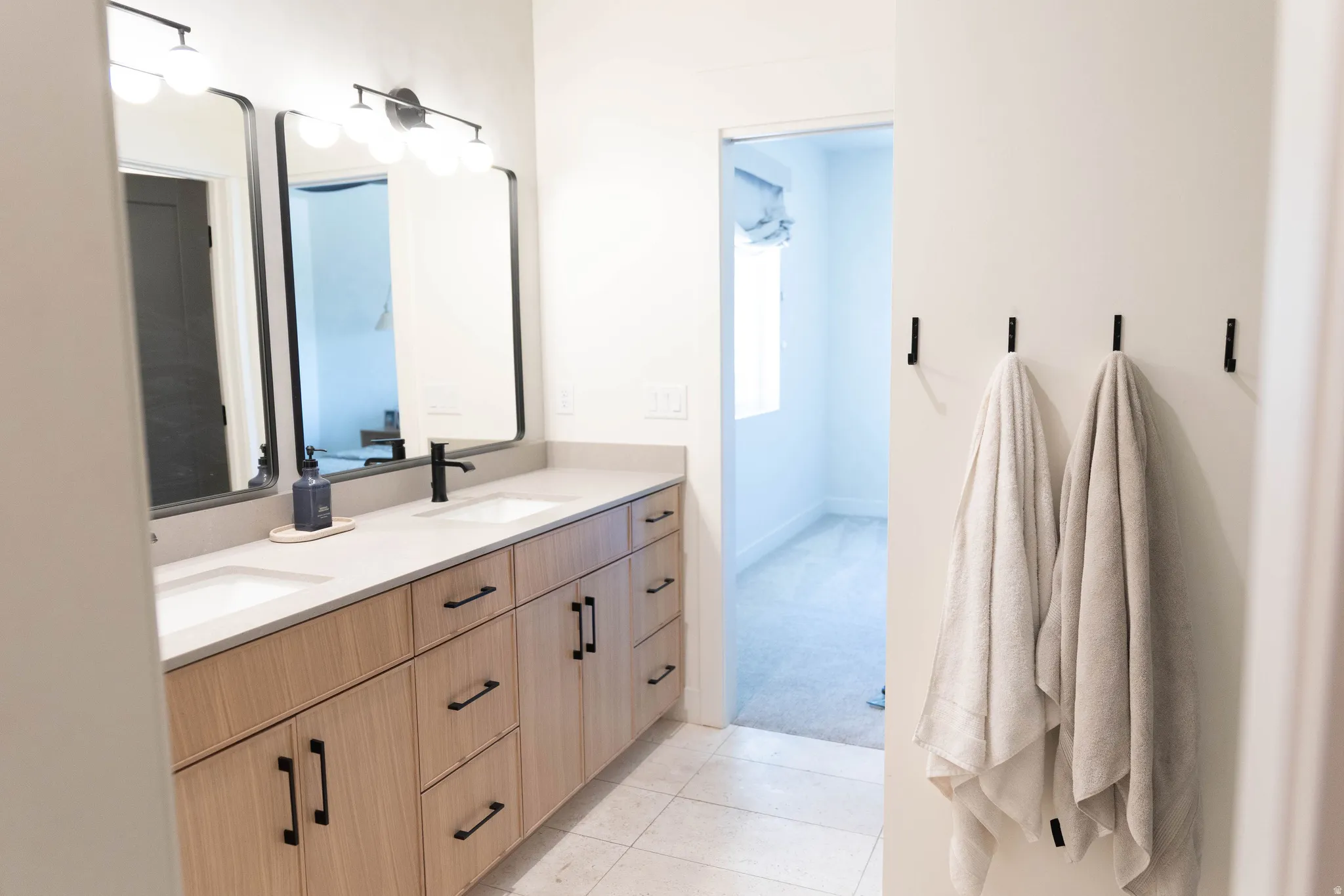 Double vanity featuring light wood-finish cabinetry with matte black hardware, dual undermount sinks, and light-toned countertops