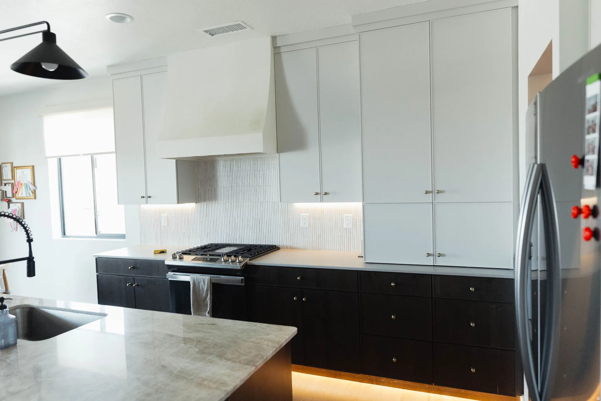Modern kitchen featuring a gas range, white shaker cabinetry, dark base cabinetry, a stone-finish island countertop, and a stainless steel sink with a matte black faucet