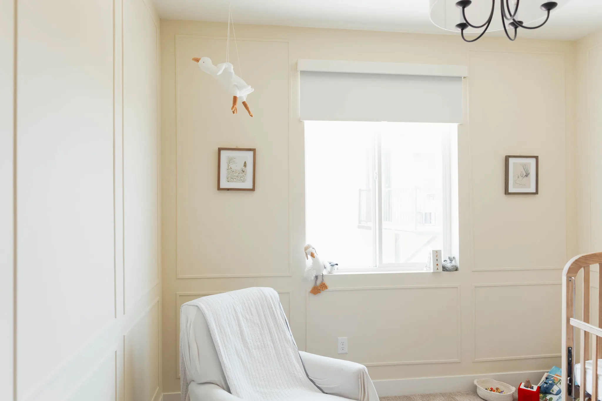 Room featuring full-height wainscoting with decorative trim, a large window with a roller shade, and a flush-mount chandelier with black iron arms