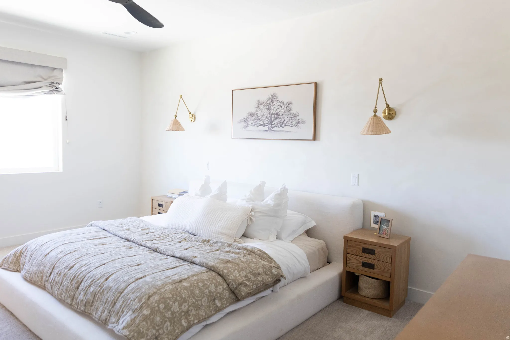 Bright bedroom featuring a flush-mounted ceiling fan, a window with a roman shade, and wall-mounted sconces
