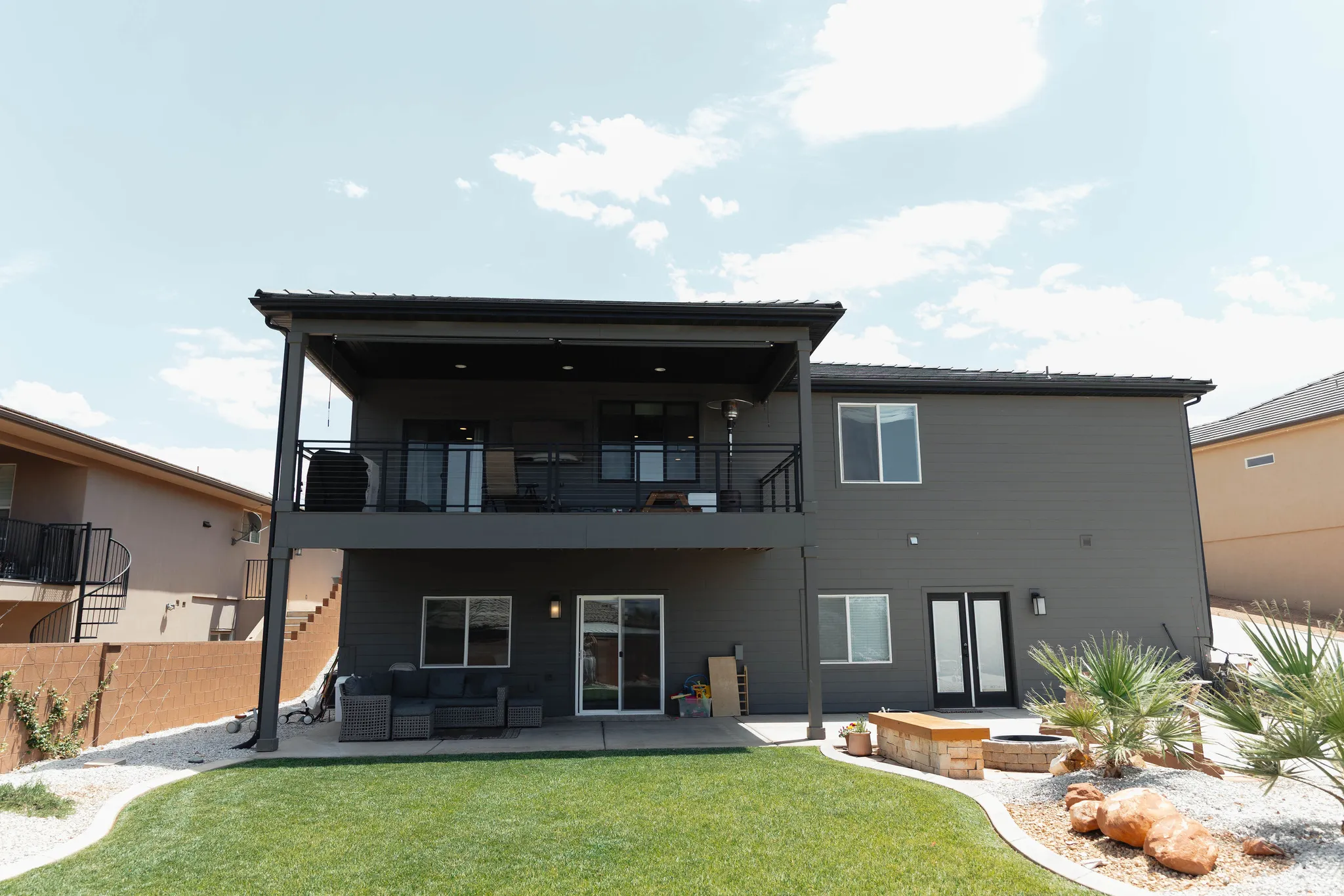 Rear exterior featuring a covered upper-level balcony with black railing, a ground-level patio, and a manicured lawn