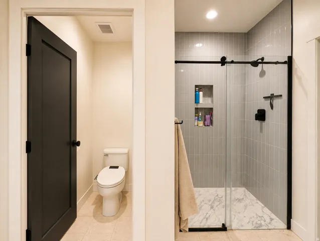 Walk-in shower with vertical tile surround, built-in shelving, and a marble-patterned base