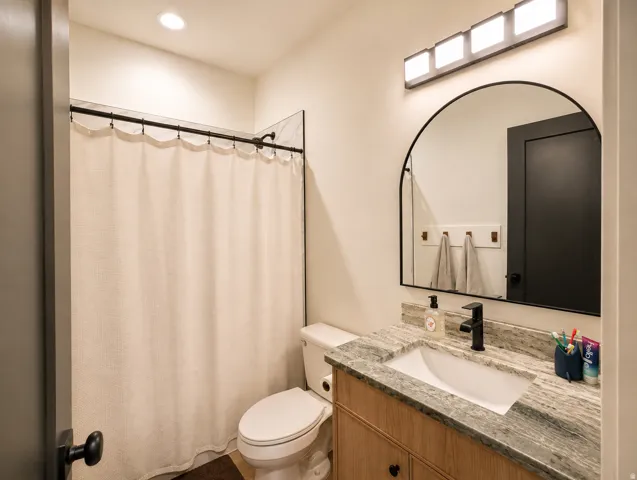 Bathroom featuring a wood-finish vanity with a stone countertop, an integrated sink, a contemporary black faucet, and an arched mirror