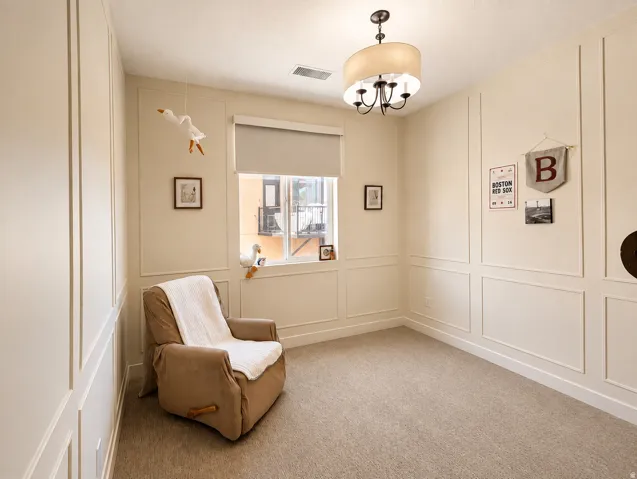 Wall paneling, neutral carpeting, recessed window with roller shade, and a drum-shade chandelier