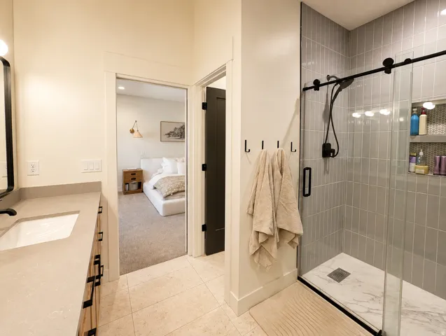 Bathroom featuring a shower with gray subway tile surround and a glass enclosure, light-toned floor tiling, a vanity with an undermount sink, and wood-finish cabinetry