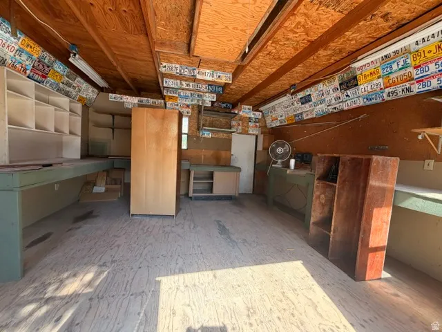 Spacious utility area featuring exposed wood beam ceiling, wood-finish flooring, and extensive built-in shelving and workbench space