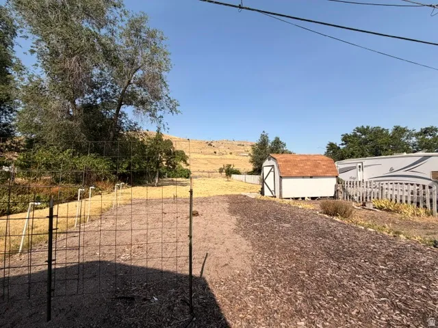 Expansive outdoor space featuring a mulched pathway, a white storage shed with a brown shingle roof, and a sloped, treed landscape in the background