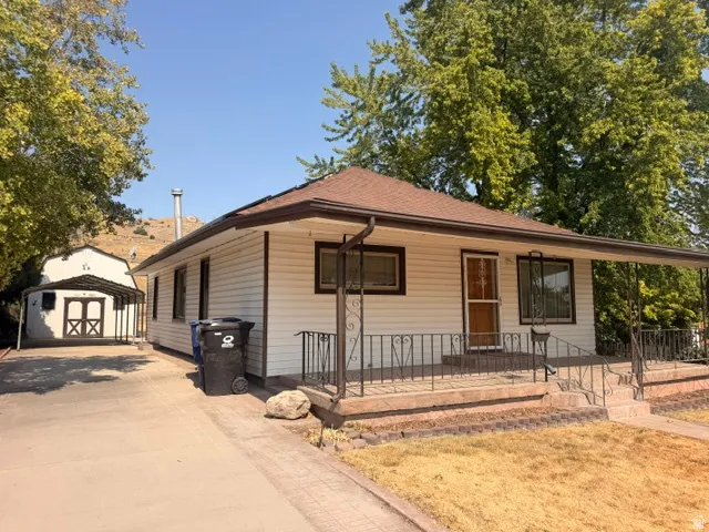 White siding home with a brown shingle roof, a front porch featuring black wrought iron railings, and a concrete driveway