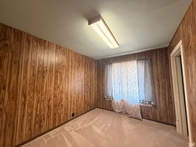 Room featuring wood-finish paneling, a textured ceiling, and neutral carpet flooring