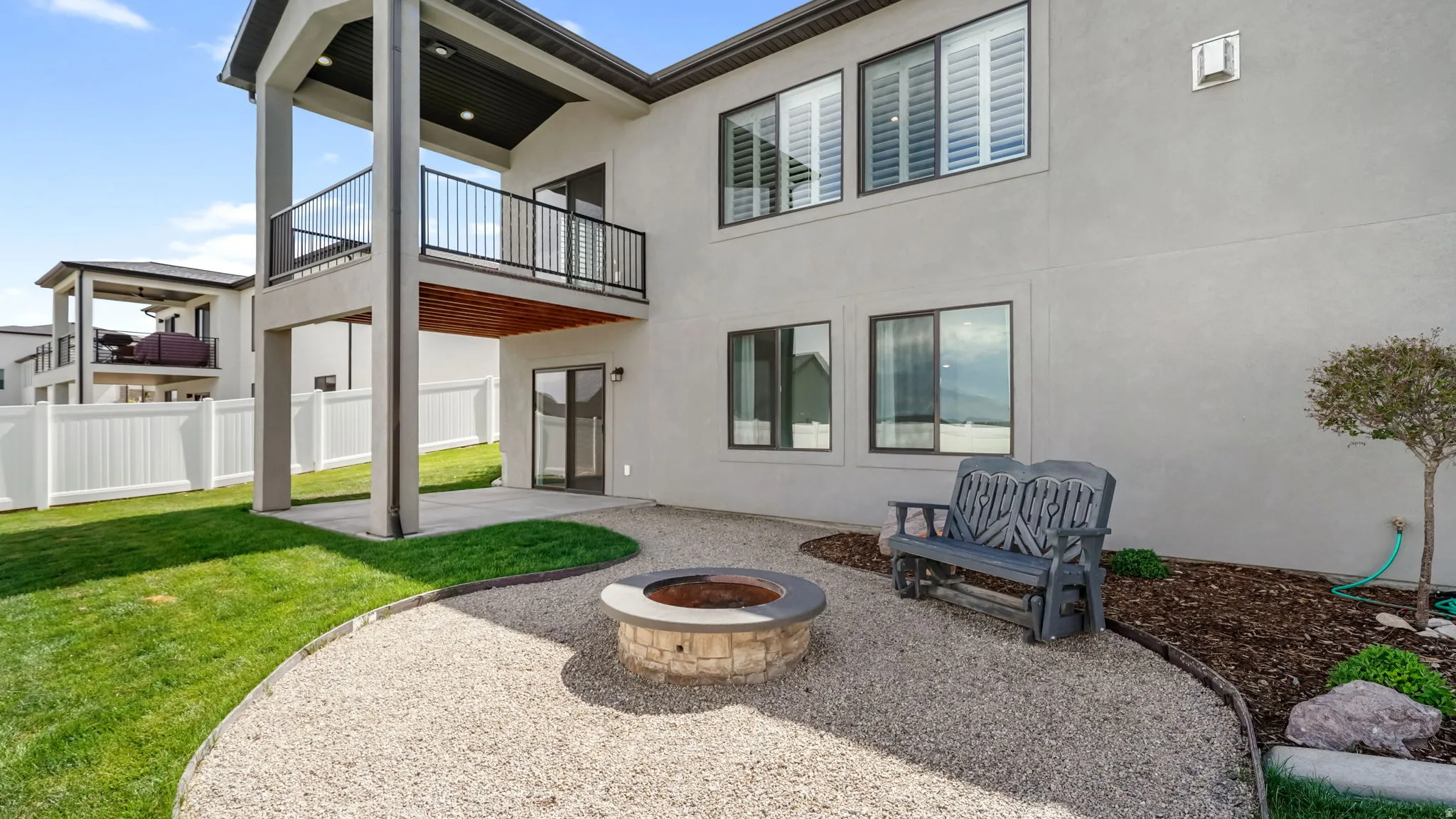 Expansive rear yard featuring a gravel patio with a built-in fire pit, a covered concrete patio, and a manicured lawn