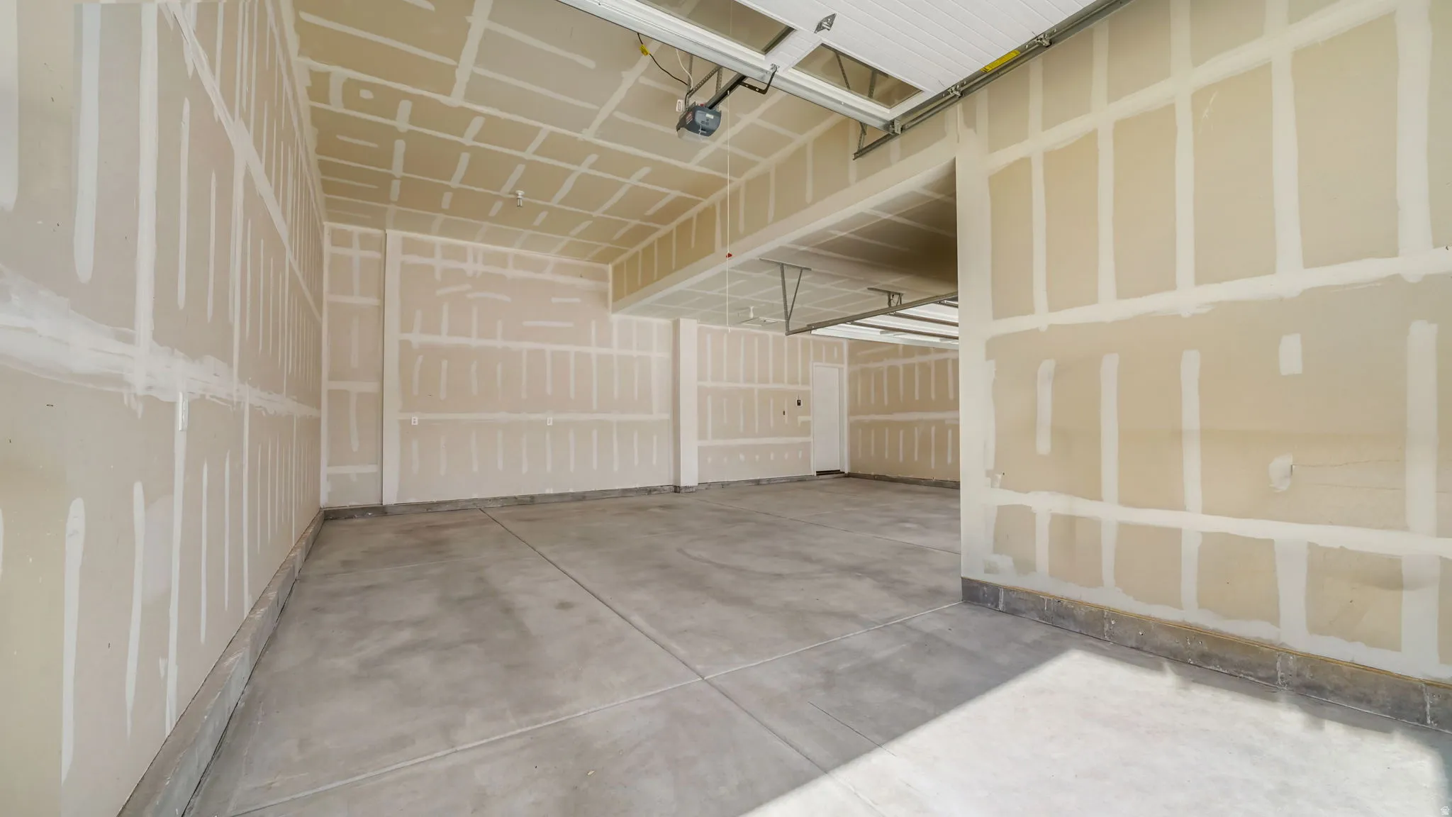 Expansive three-car garage featuring exposed drywall, concrete flooring, and an overhead garage door