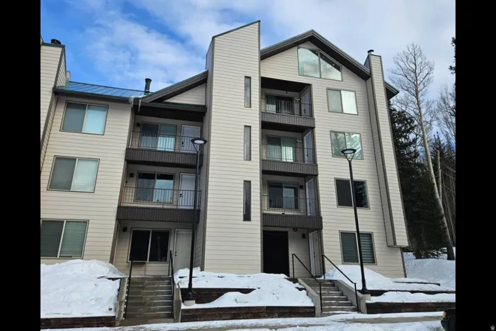 Multi-story building featuring light-toned siding, a blue-hued metal roof, and multiple balconies with dark railings