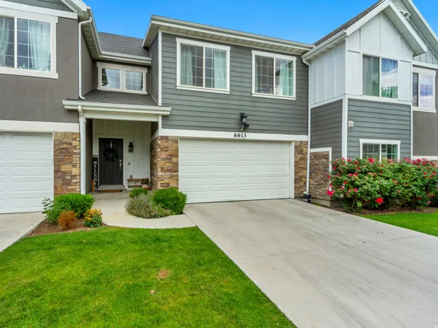 Modern townhome exterior featuring gray siding, stone veneer accents, white trim, a covered entry, and a two-car garage