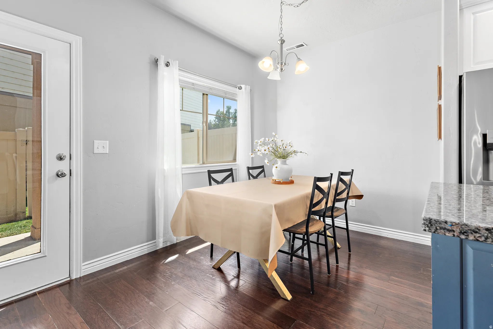 Dining area featuring wood-finish flooring, a window with sheer curtains, a three-light chandelier, and a glass-paneled door